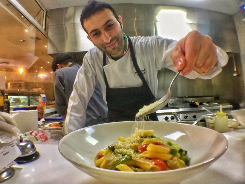 Chef topping pasta dish with cheese in kitchen.