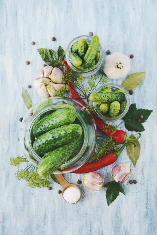 Three jars of pickles sit on a table surrounded by picking ingredients.