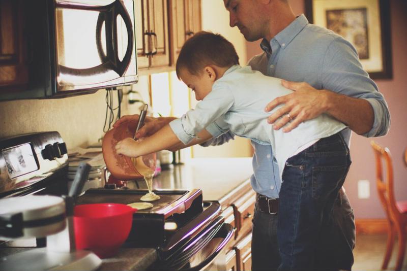 A father helping a child make pancakes.