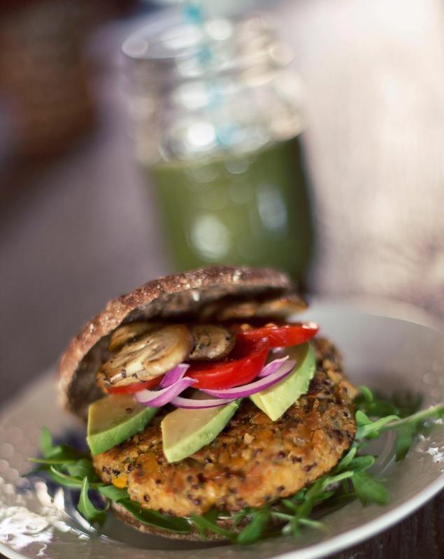 A burger topped with avocado, onion, mushrooms and bell pepper is served on a plate.