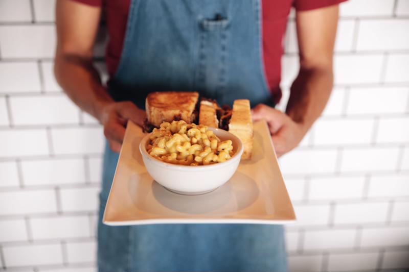 A server holding an entree dish in front of a white wall.