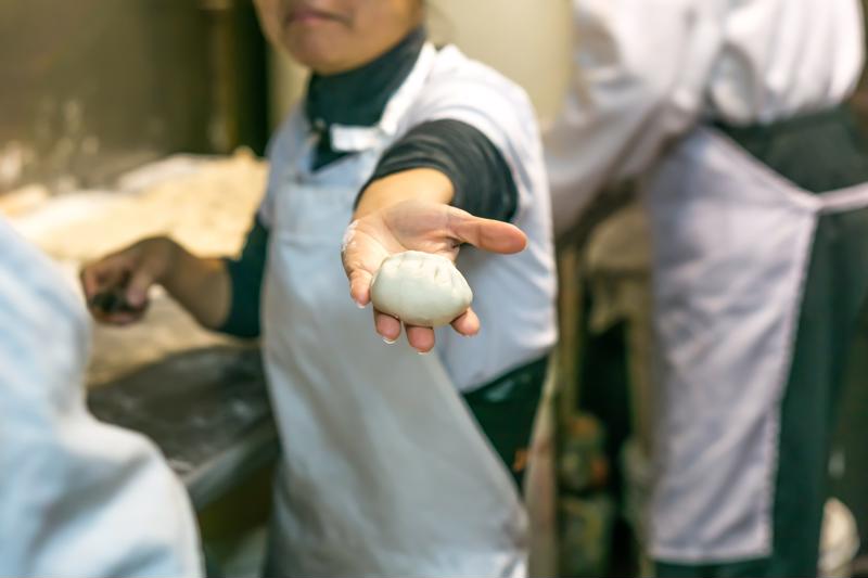 A line cook holding up a ball of dough.