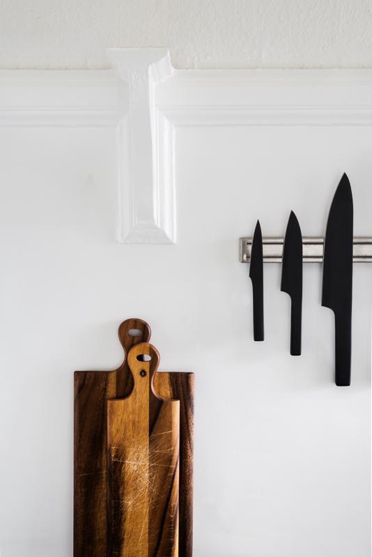 Chefs knives and wooden cutting boards are displayed in an all-white kitchen.