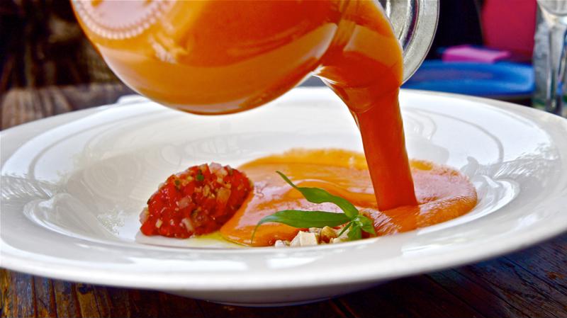 A fresh gazpacho is poured into a white bowl.