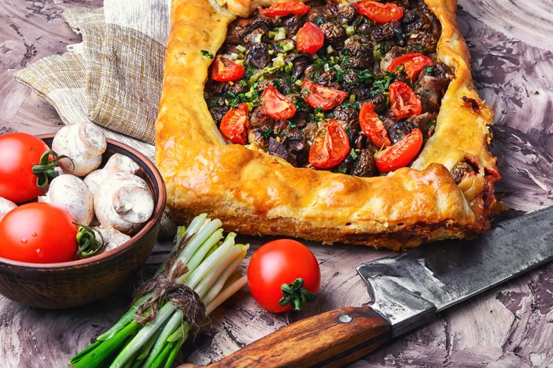 A savory pie alongside ingredients and a kitchen knife.