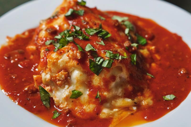 A piece of lasagne in sauce, sitting in a bowl.