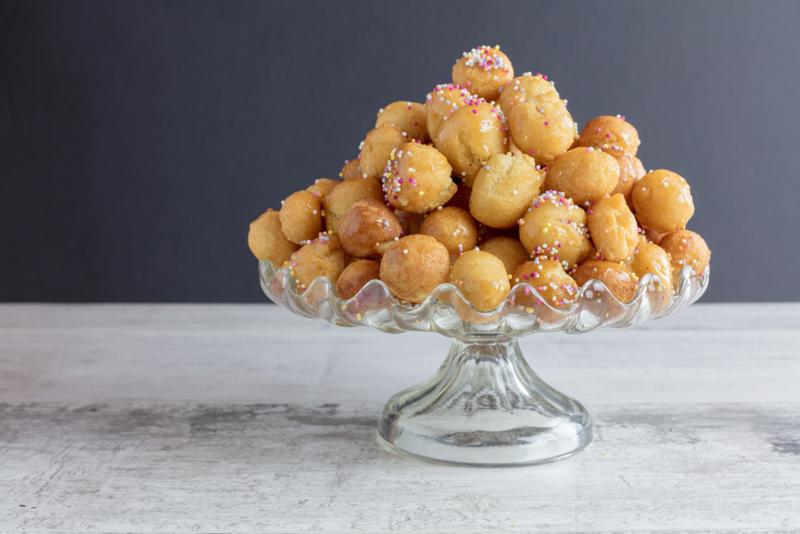 Struffoli with sprinkles in a glass dish.