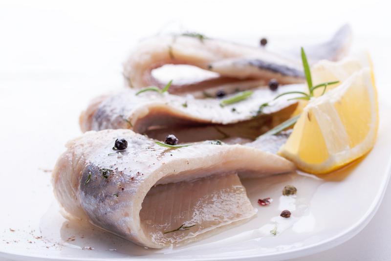 Three pieces of pickled herring served on a white plate.