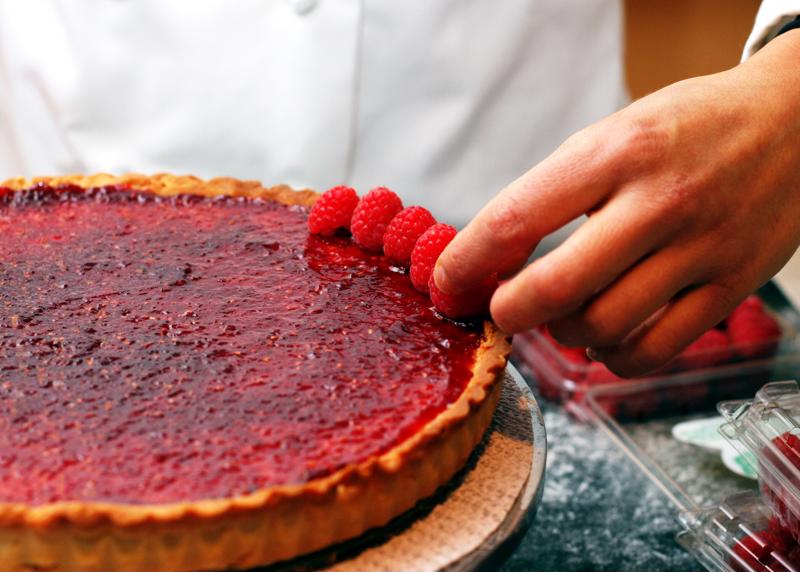 A pastry chef adding raspberries to a dessert.
