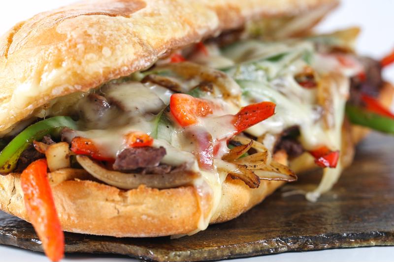 A close up of a hot sandwich with vegetables, steak and melted cheese.