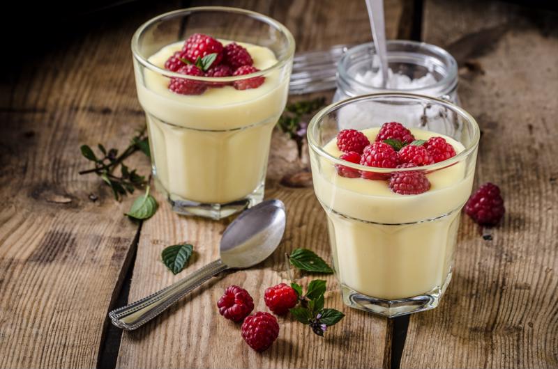 Vanilla pudding and raspberries in two glasses.