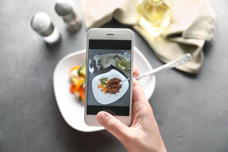 A chef taking a photo of a plated dish on a smartphone.