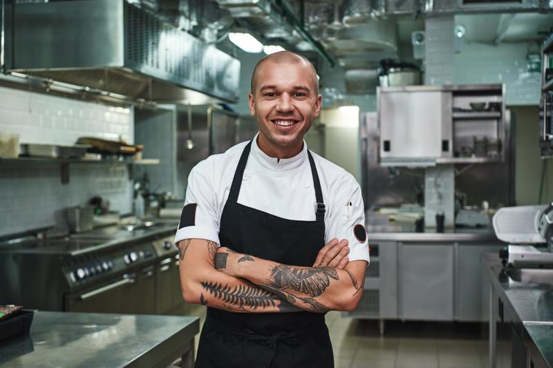 A chef standing in a kitchen, smiling at the camera with arms crossed.